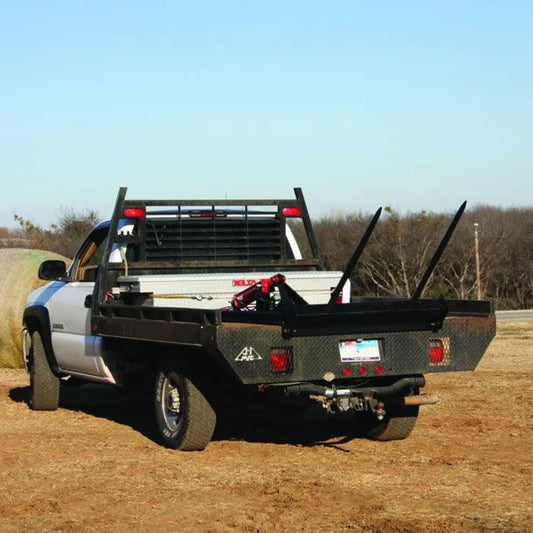 A PIERCE Bolt-in Hydraulic Truck Bed Hay Bale Spear-equipped pickup truck is parked on dirt near a field, ready for efficient hay bale transport.