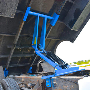 A blue hydraulic lift, powered by a 12V hydraulic pump, raises the bed of a dump truck with the PIERCE Light Duty Flat Bed Dump Kit, exposing the chassis and underside.