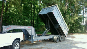 A white truck equipped with a PIERCE Light Duty Flat Bed Dump Kit and a 12 Volt hydraulic pump is tilted up to unload by trees and a gravel lot.