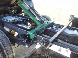 The PIERCE Light Duty Flat Bed Dump Kit features a hydraulic lift mechanism with a 12V pump, mounted on a vehicle chassis with detailed metal framework and cylinders—perfect for flatbed dumping applications.