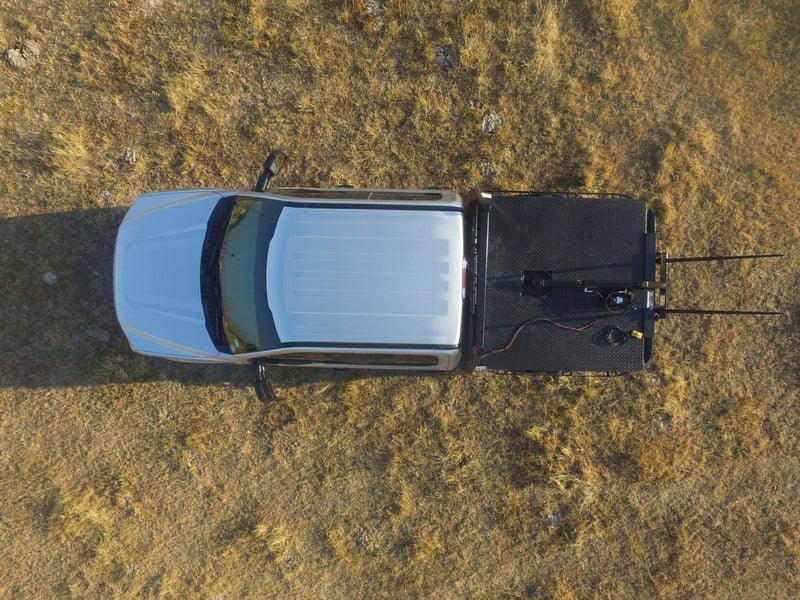 Top view of a white truck with a PIERCE Truck Bed Gooseneck Hay Bale Mover mounted on its flatbed, parked on dry grass.