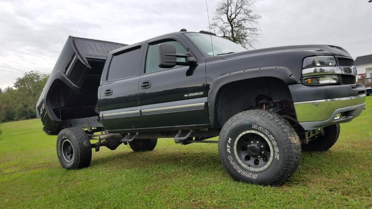 A lifted black pickup truck, fitted with the PIERCE Factory Bed Dump Kit, sits on a grassy area under a cloudy sky, showcasing its impressive lifting strength.