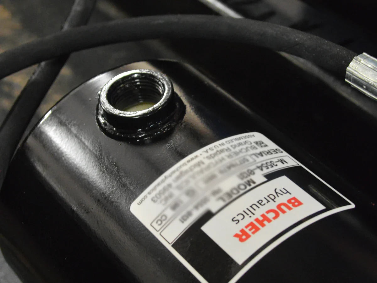 Close-up of a Bucher Hydraulics cylinder with a threaded port and attached black hydraulic hose.