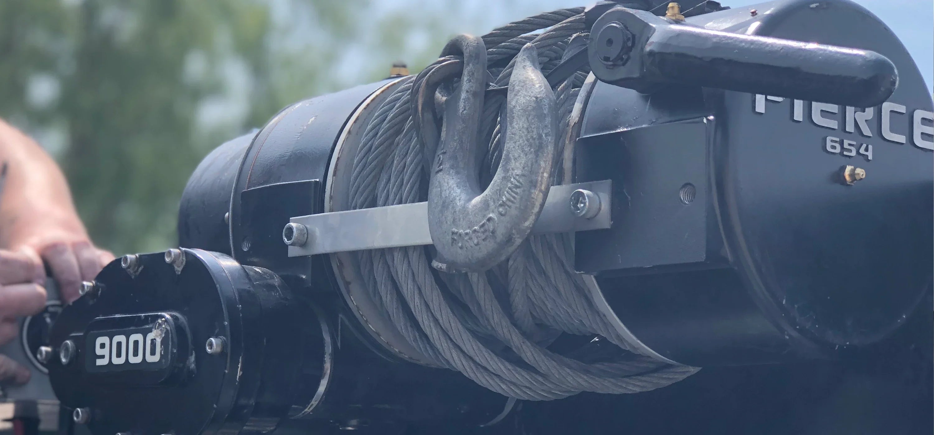 Close-up of a winch with a coiled steel cable and hook labeled Pierce 654 and 9000.