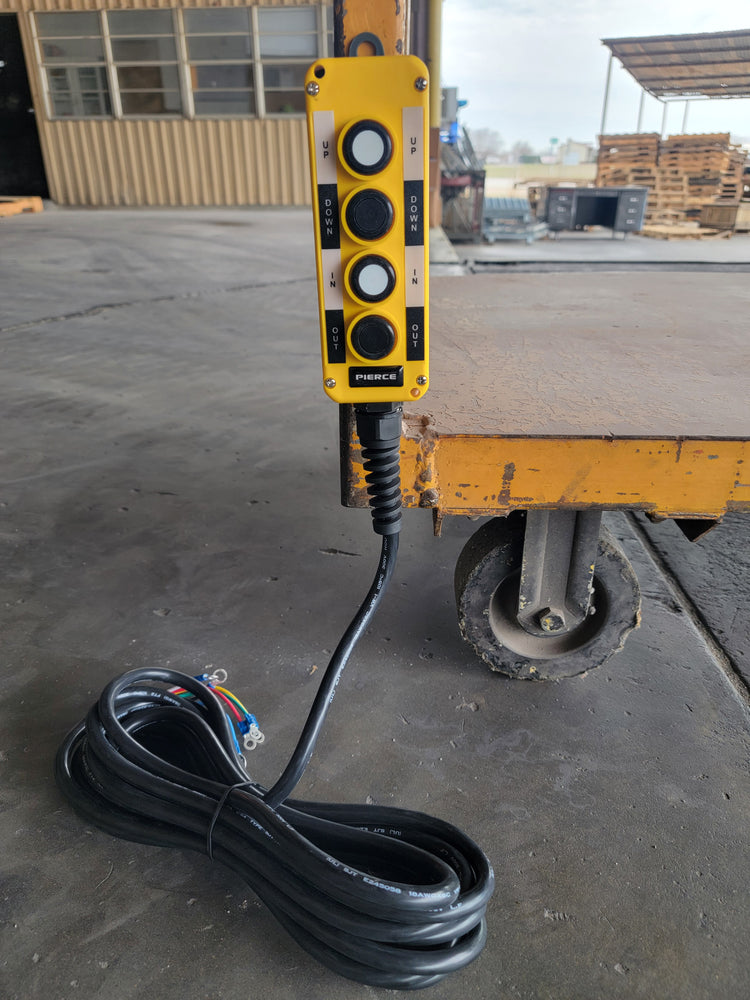 A PIERCE Universal Momentary Pendant Control with four buttons and a 20ft cord, enhanced with magnets, lies on the warehouse floor near a wheeled cart.