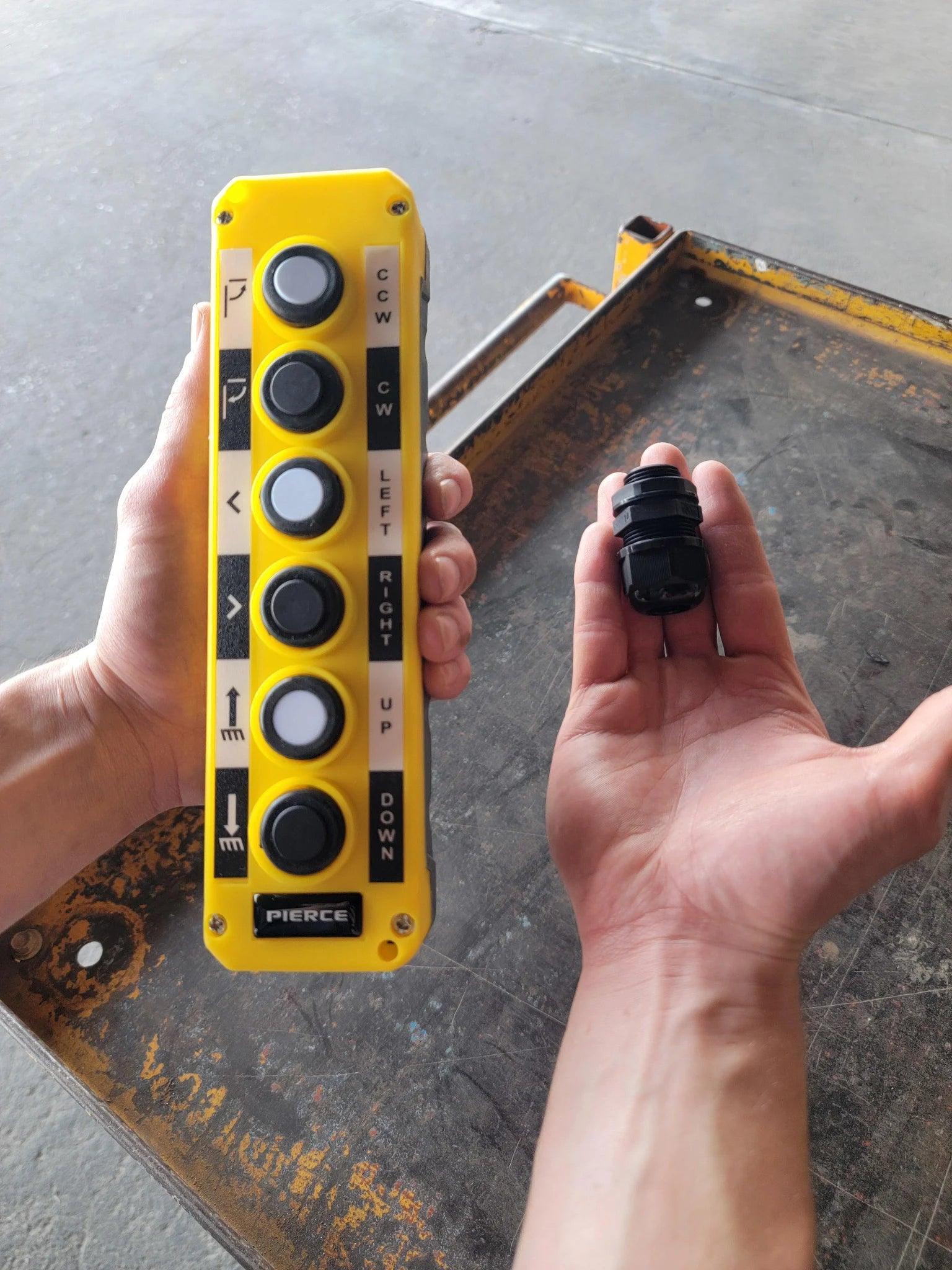 A person holds an Asetek Enterprise Company LTD Universal Momentary Pendant Control - 6 Button with a black connector over a metal surface, typically used to operate hydraulic power units.