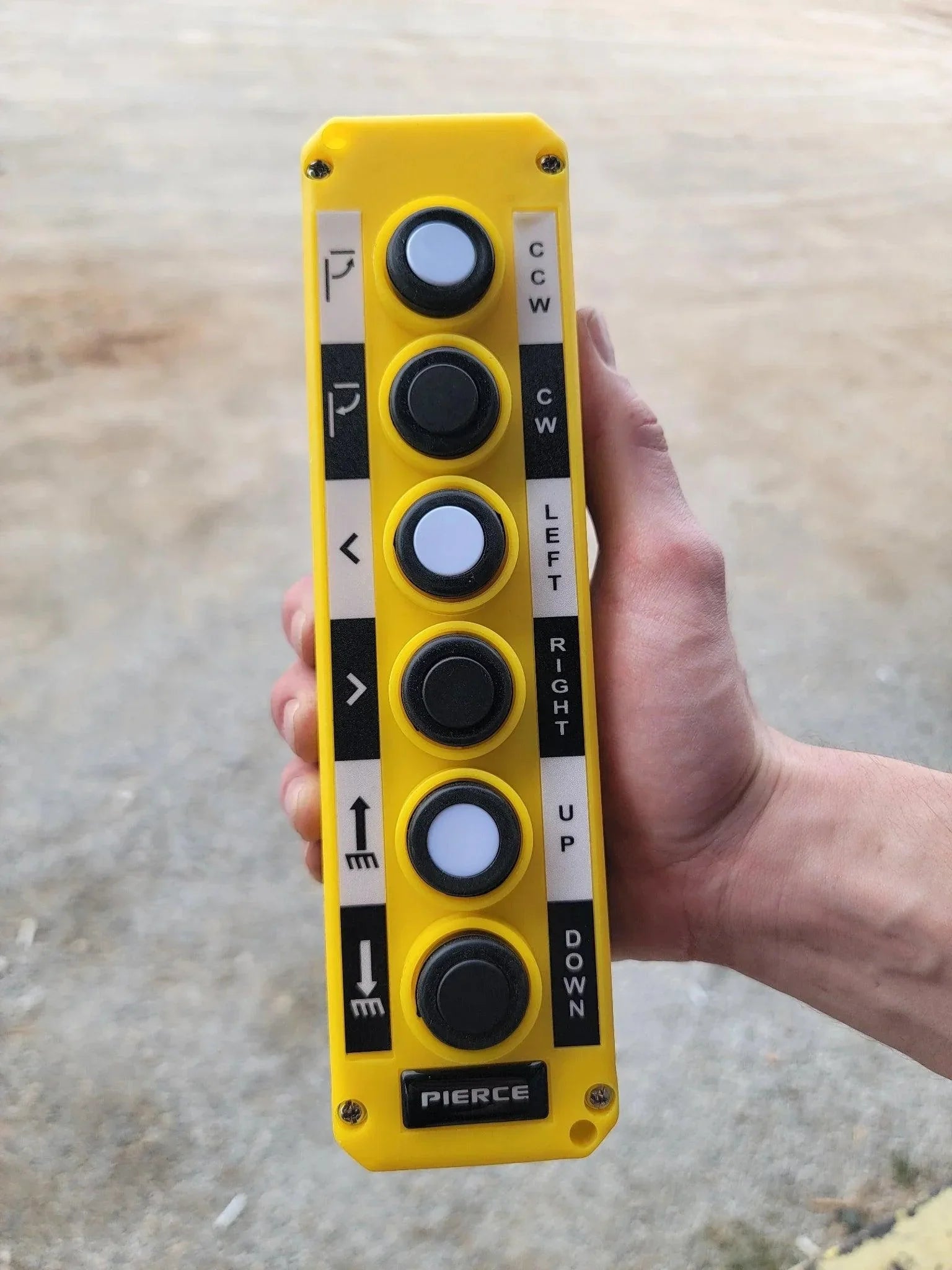 A hand holds the Asetek Enterprise Company LTD Universal Momentary Pendant Control – 6 Button, a yellow replacement controller commonly used for operating hydraulic power units.