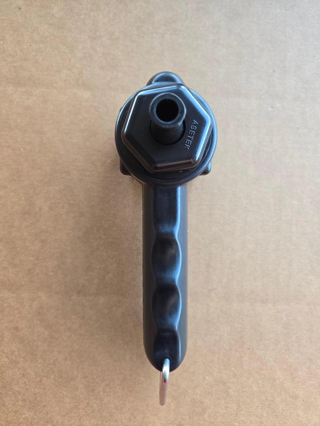 PIERCE Universal Toggle Switch Remote - No Cord by PIERCE features a black plastic hexagonal handle with a hole, ideal as a replacement pendant for toggle switch remote systems. Shown on a light brown textured surface.