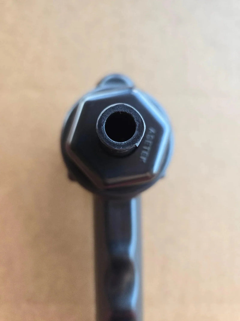 Close-up of the PIERCE Universal Toggle Switch Remote - No Cord by PIERCE, a black hexagonal device with a central hole, viewed from above on a tan background.