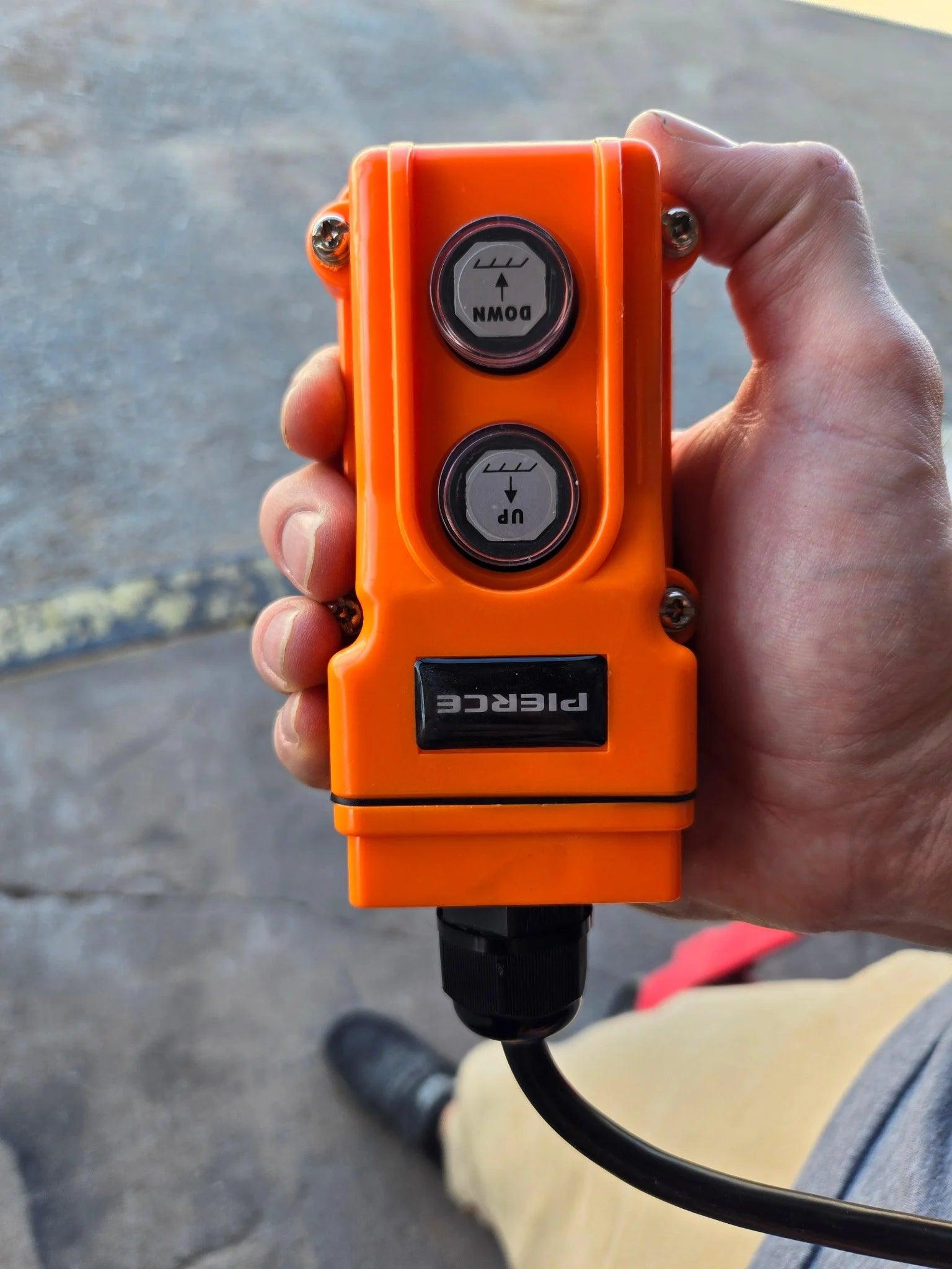 A hand holds an Asetek Enterprise PIERCE 2 function Momentary Hard-Wired Control Pendant—15 ft. cord, 4-prong vulcanized plug, UP/DOWN buttons—commonly used to operate wormgear winches.