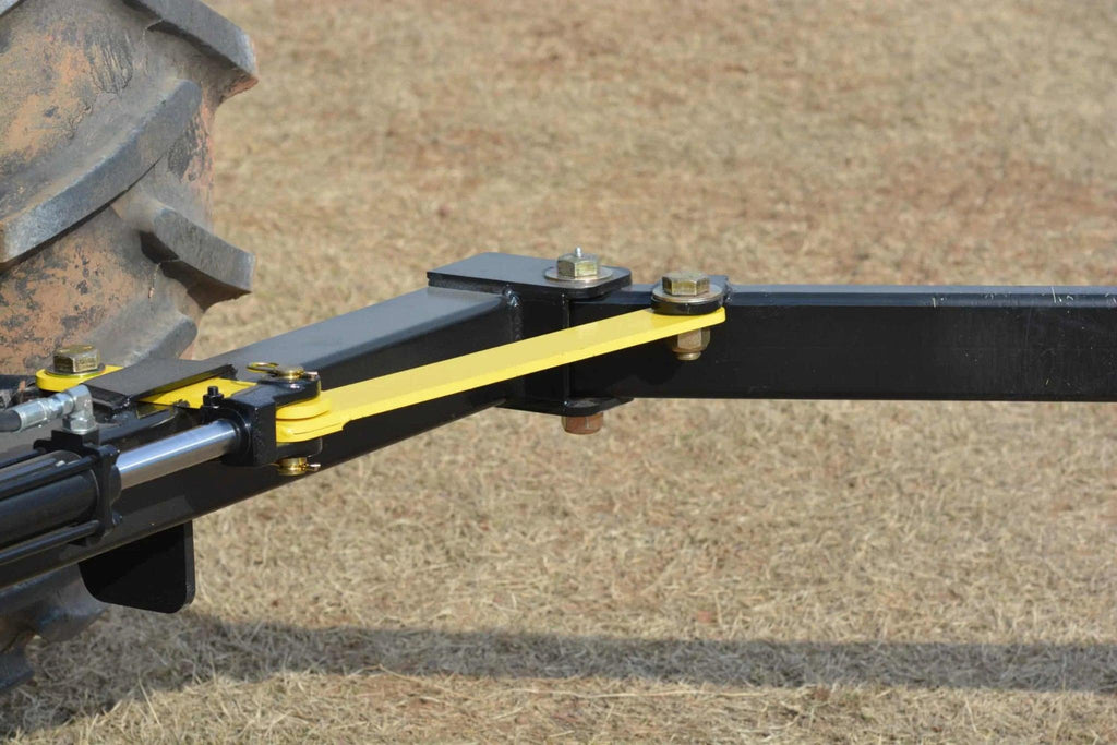Close-up of a tractor hitch with a yellow stabilizer bar on dry grass, ideal for attaching the Internal - Pierce Assembly Team 3-Point Hay Bale Unroller.