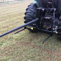 A tractor with a black Internal - Pierce Assembly Team 3 Point Tractor Bale Spike sits on grassy ground, ready for moving and handling round hay bales.