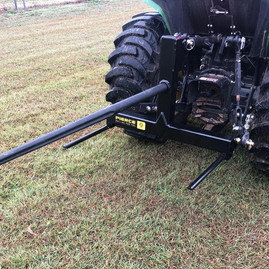 A PIERCE 3 Point Tractor Bale Spike with a black hitch attachment is set on the grassy field, perfect for handling round bales effortlessly.