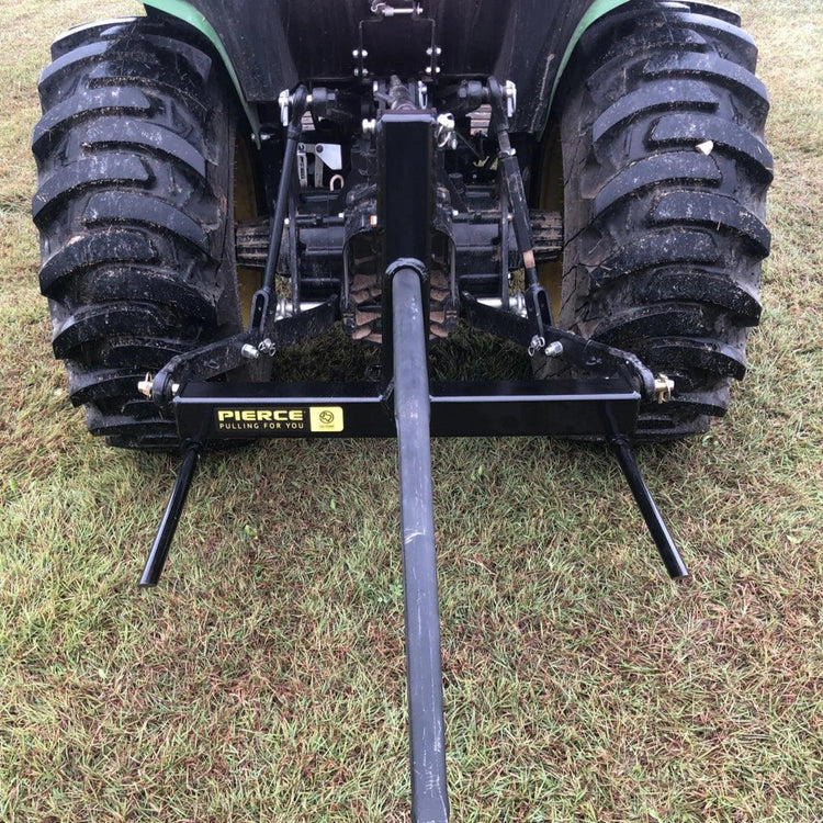 A rear view of a tractor parked on grass displays the PIERCE 3 Point Tractor Bale Spike, featuring a durable black towing frame made of high-quality steel, designed to handle round bales efficiently.
