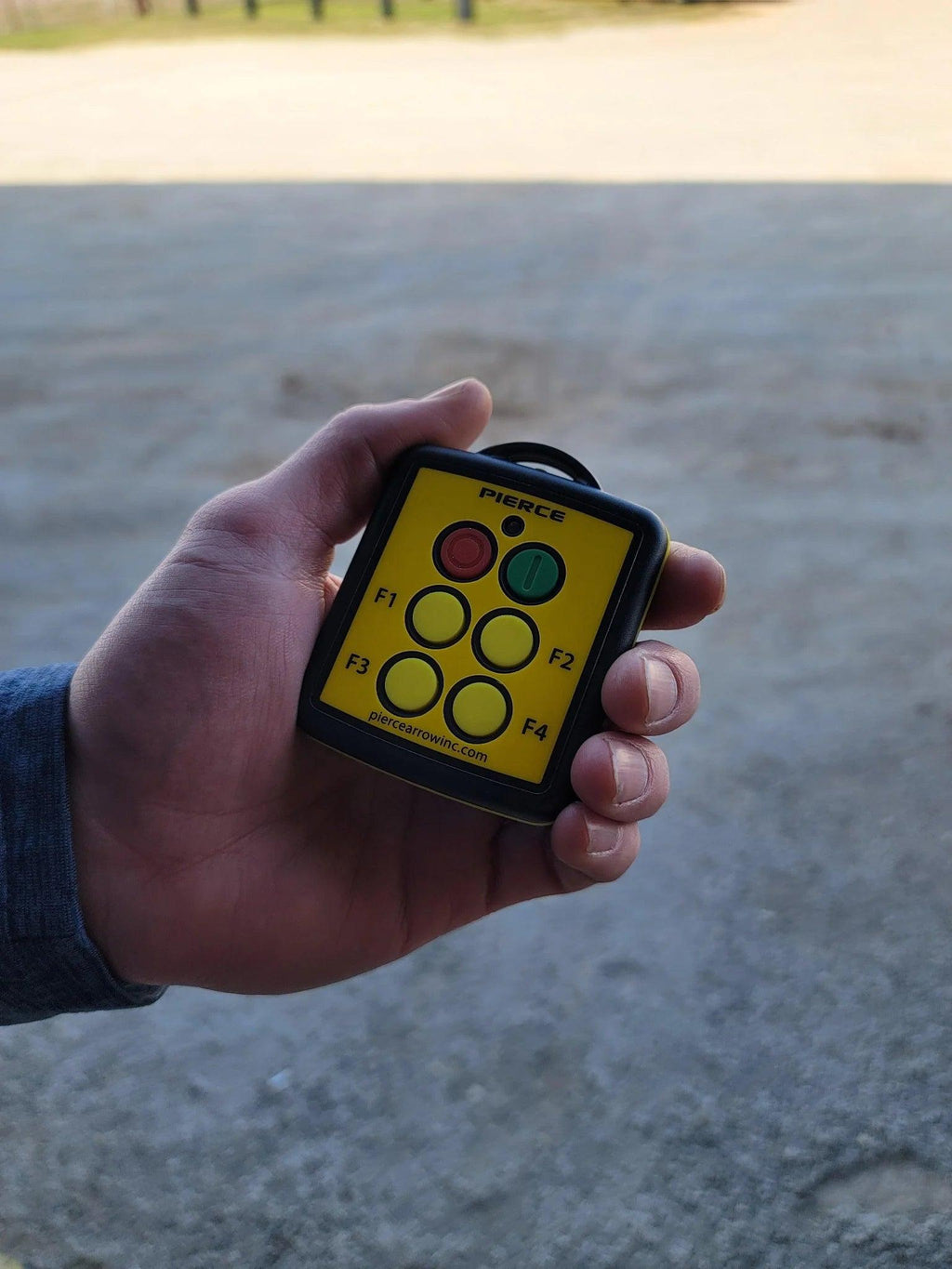 A hand holds a Lodar LTD 4 Function Wireless Remote Control System with labeled buttons outdoors.