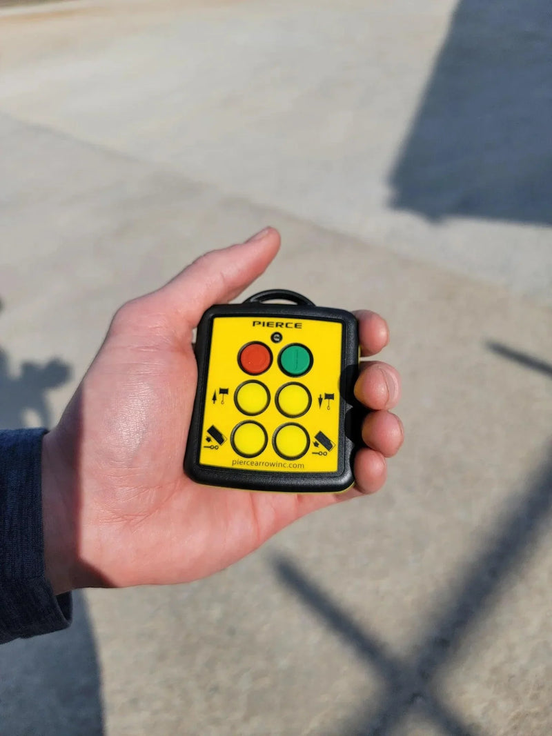 A hand holds the Lodar LTD 4 Function Wireless Remote Control System | Roll-off Trailer Edition, a compact yellow device used to operate roll-off trailers or hydraulic pumps.