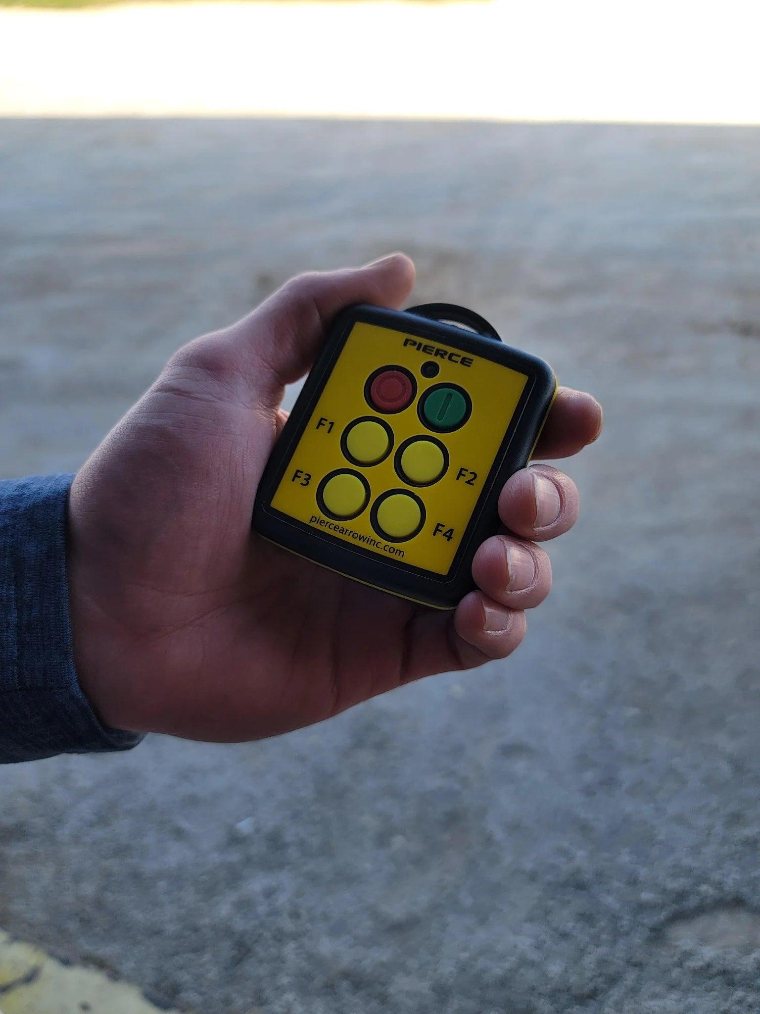 A hand holds a Lodar LTD 4 Function Wireless Remote Transmitter, featuring labeled F1–F4 buttons plus green and red, all marked with the brand name.
