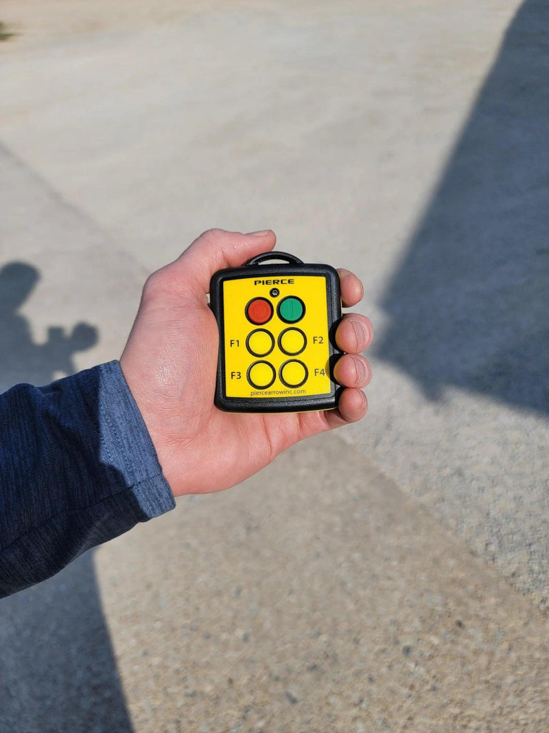 A hand holds a Lodar LTD 4 Function Wireless Remote Transmitter with six buttons labeled F1 to F4, used for equipment control.