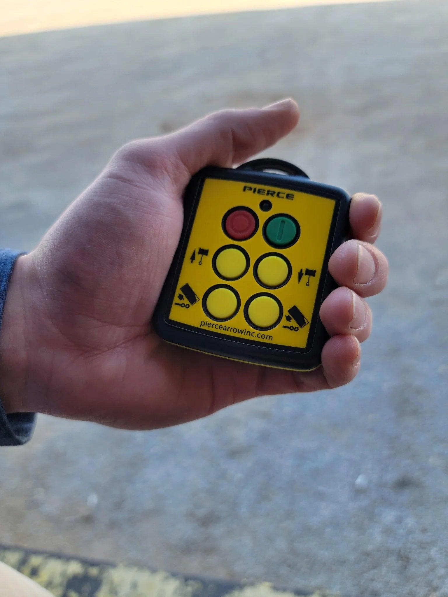 A hand holding a Lodar LTD 4 Function Wireless Remote Transmitter, a compact yellow device with buttons and directional arrows, designed as part of a wireless remote system.