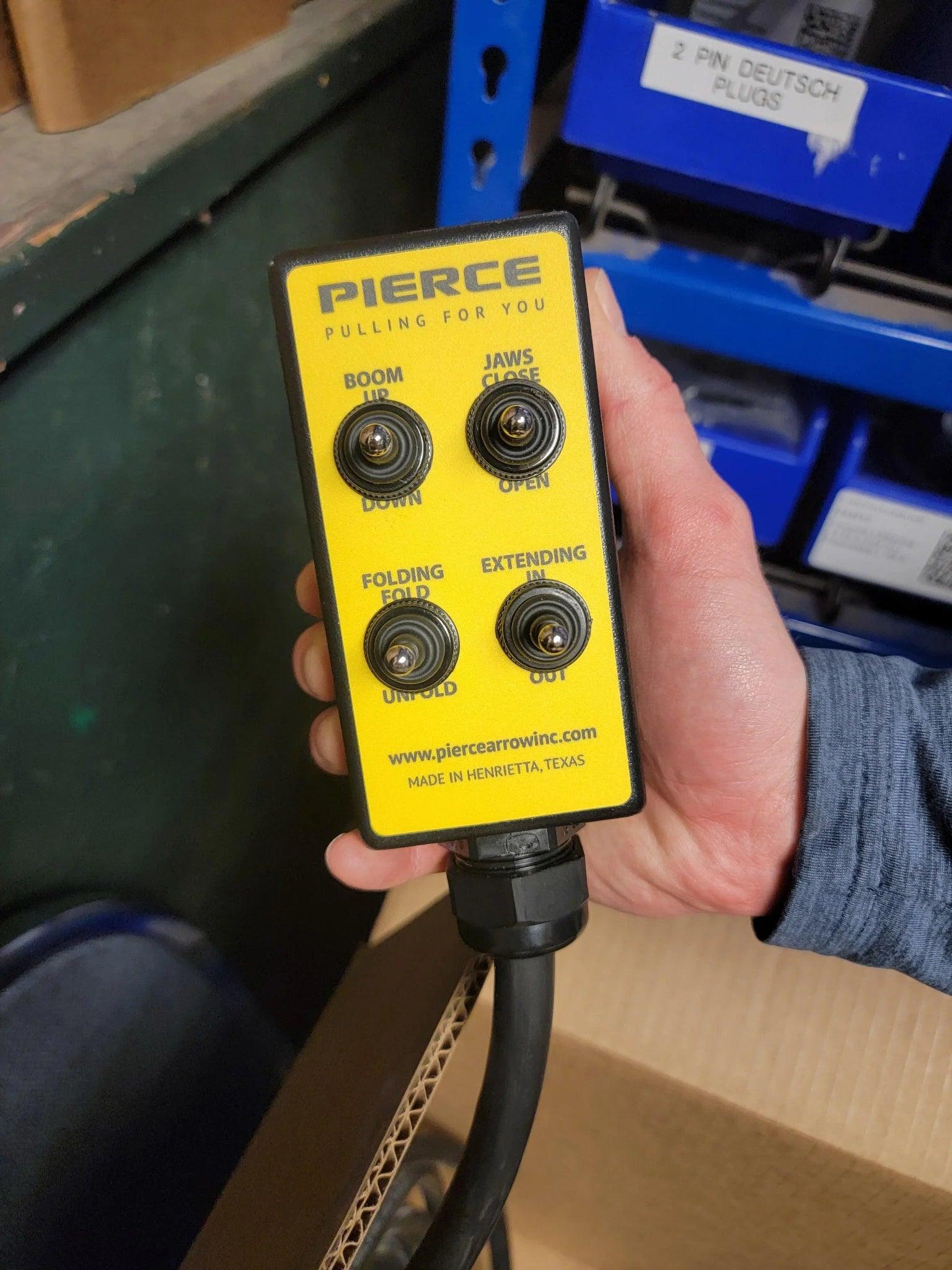 Hand holding a yellow PIERCE 8 Function Wrecker Remote with labeled switches for boom, jaws, folding, and extending—perfect for 12/24V solenoid systems and hydraulic power units.