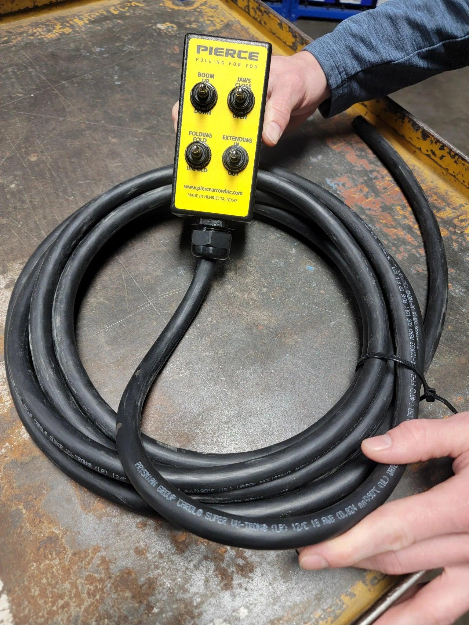 A person holds a black coiled cable with a yellow PIERCE control box. It features the 8 Function Wrecker Remote, perfect for solenoid systems in towing, and includes an intuitive toggle switch wired remote for seamless operation.