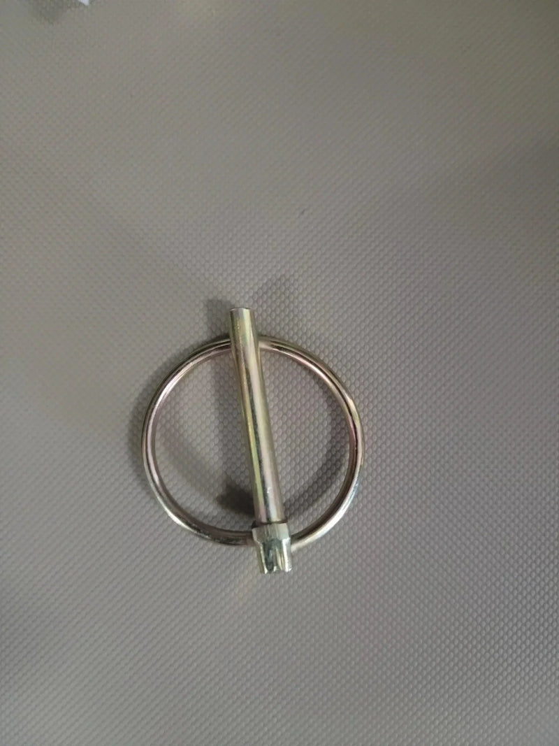A PIERCE Bale Unroller Extension Set metal lynch pin with a round ring rests on a textured gray surface.