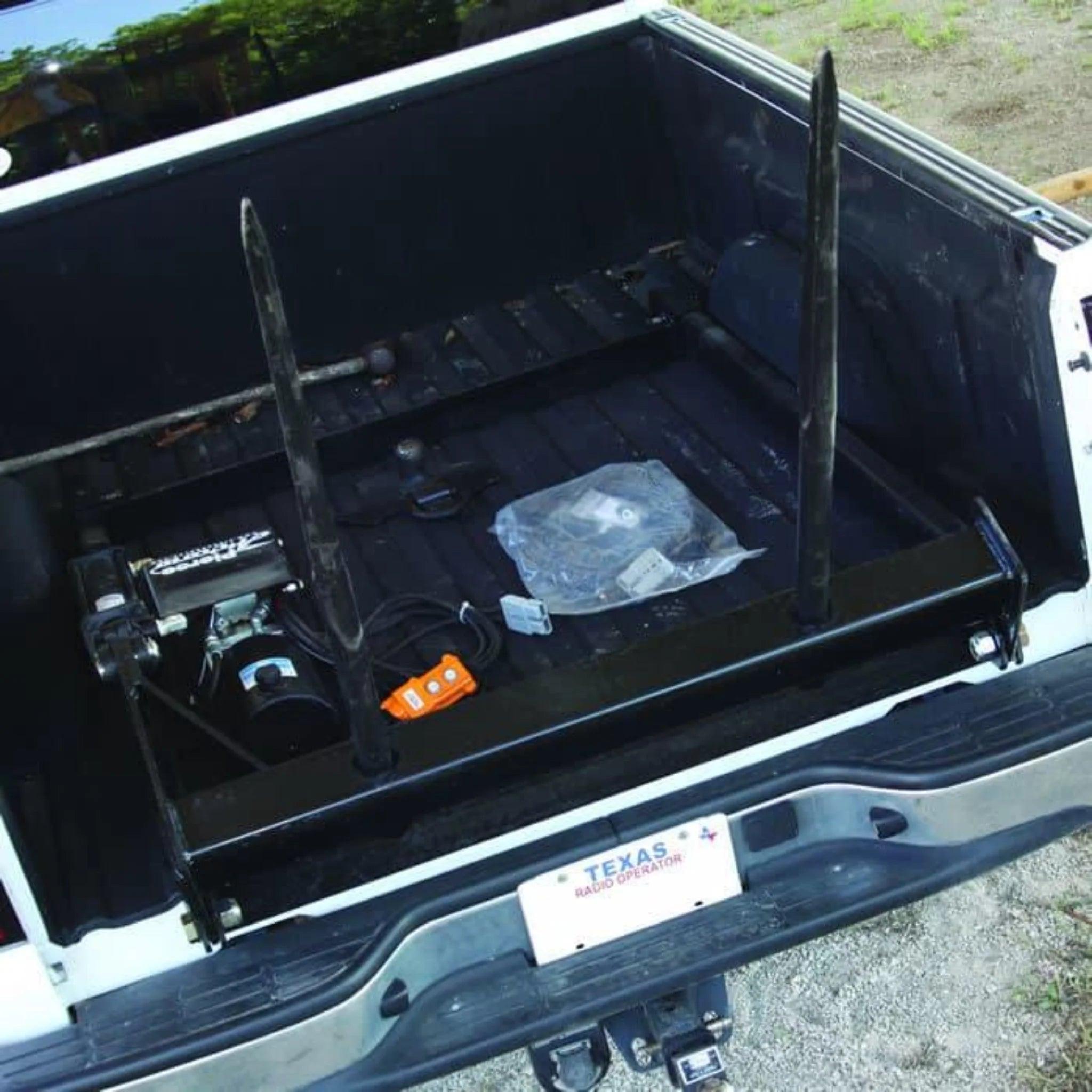 Open truck bed with metal frame, tools, a control switch, PIERCE Bolt-in Hydraulic Truck Bed Hay Bale Spear, and a visible Texas license plate.