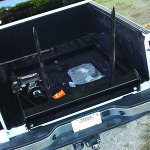 Open truck bed with metal frame, tools, a control switch, PIERCE Bolt-in Hydraulic Truck Bed Hay Bale Spear, and a visible Texas license plate.