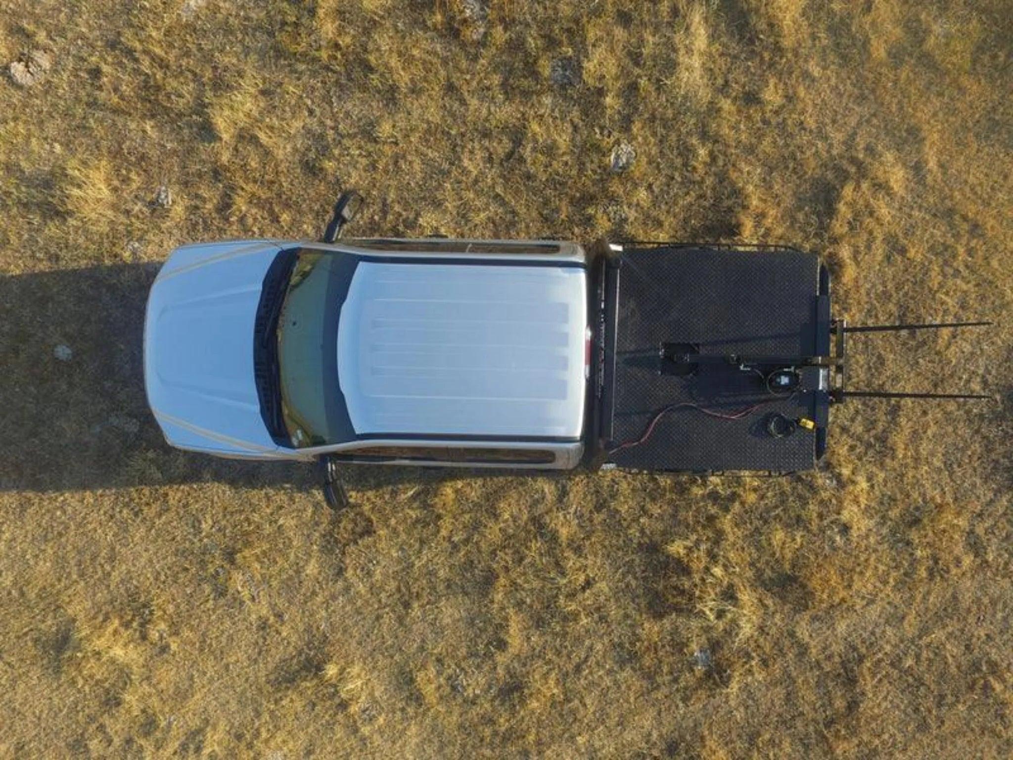 Aerial view of a white pickup truck equipped with a PIERCE Truck Bed Gooseneck Hay Bale Mover parked on dry grass.