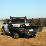 A white pickup truck with a PIERCE Bolt-in Hydraulic Truck Bed Hay Bale Spear is parked on dirt, framed by trees in the background.