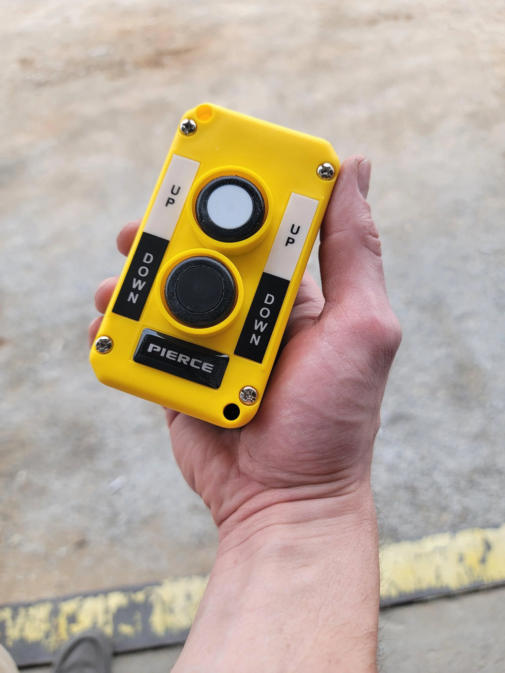 A hand holds an Asetek Enterprise Company LTD Universal Momentary Pendant Control – 2 Button, featuring yellow casing and labeled UP/DOWN buttons, commonly used with hydraulic power units in industrial applications.