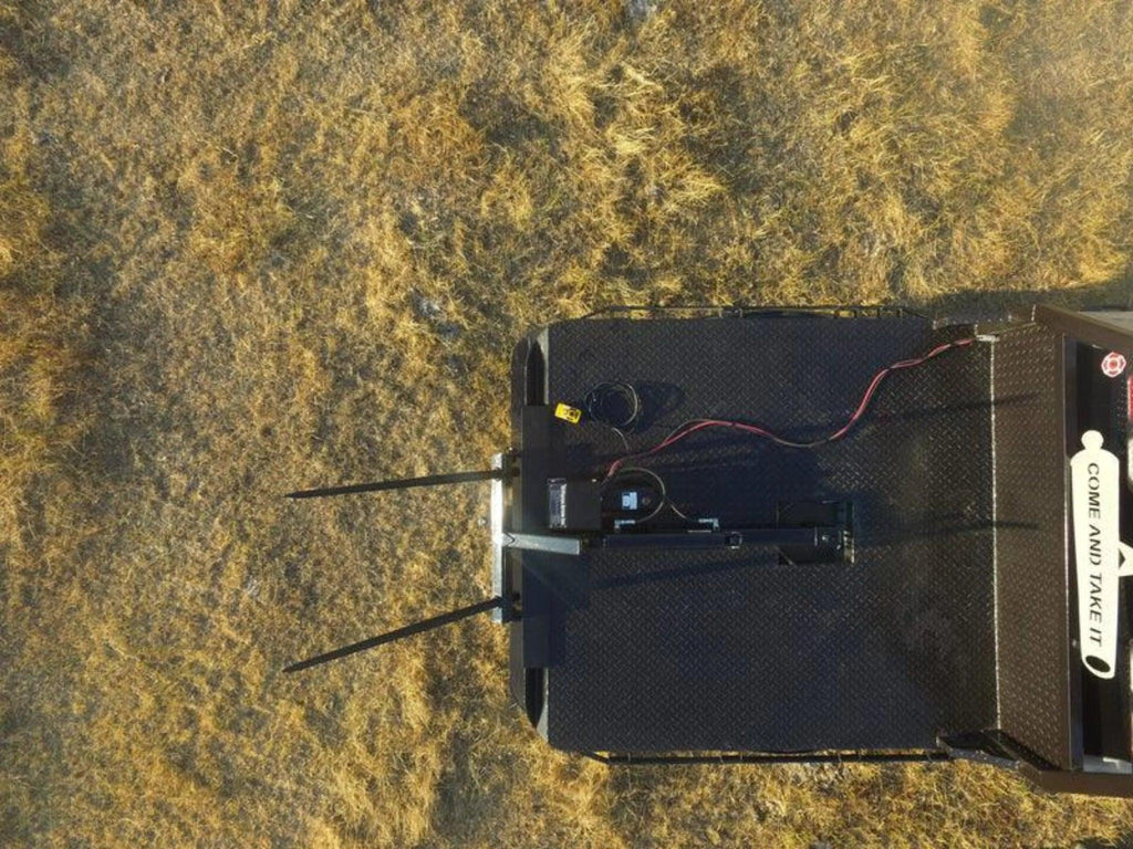 Aerial view of PIERCE Truck Bed Gooseneck Hay Bale Mover mounted on a platform in a dry grassy field, with a "Come and Take It" sticker visible.