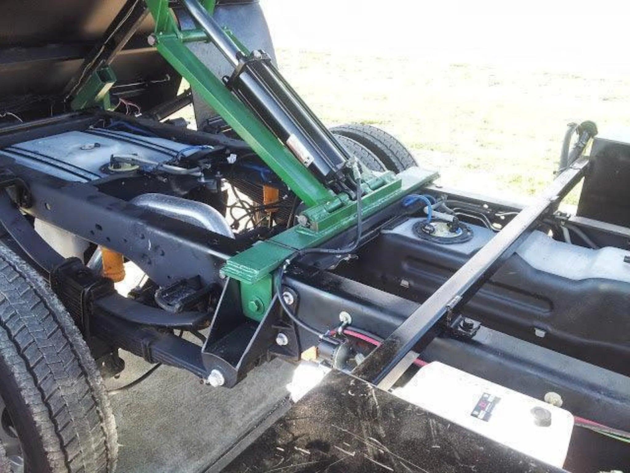 Close-up of a truck chassis featuring the PIERCE Heavy Duty Flat Bed Dump Kit with hydraulic lift mechanism attached to the frame.