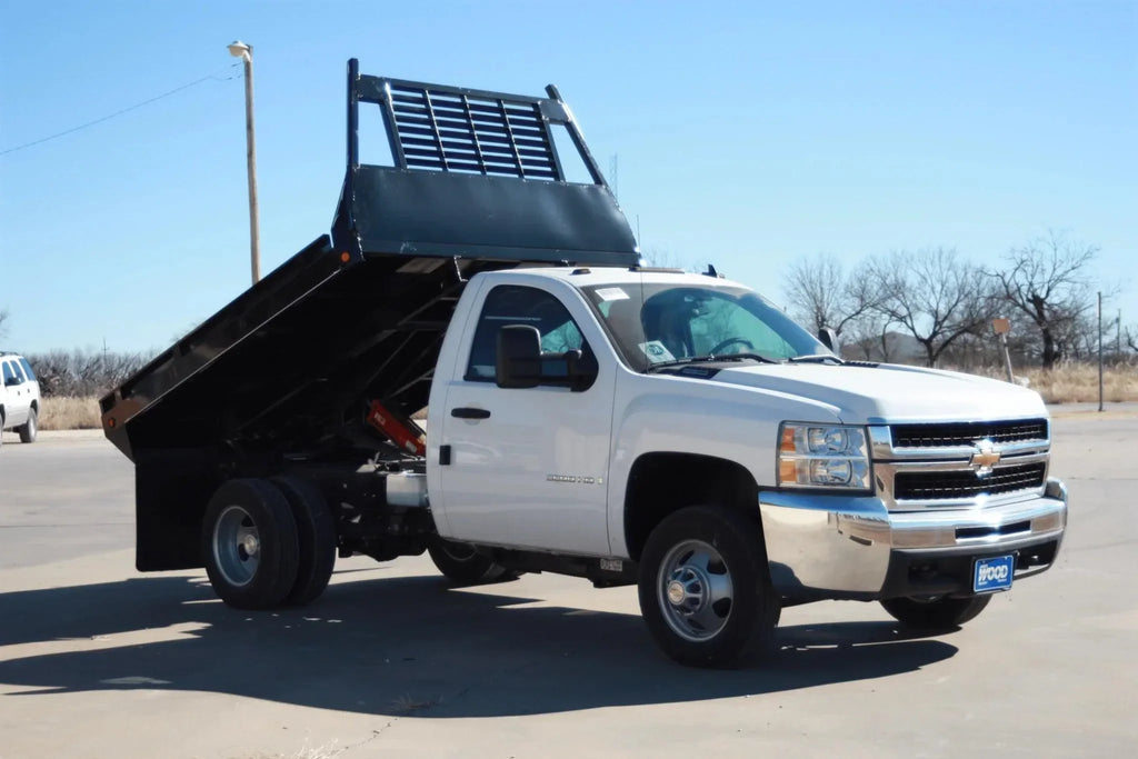 White Chevy dump truck with raised bed parked on pavement under a clear sky, equipped with the PIERCE Medium Duty Flat Bed Dump Kit for reliable and smooth operation.