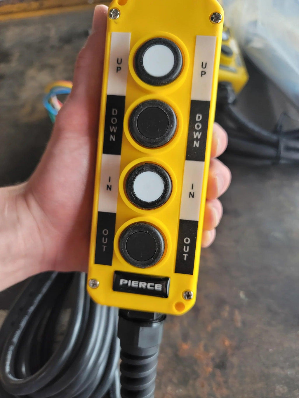 Hand holding the PIERCE Universal Momentary Pendant Control, a 4-button unit with a 20ft cord and magnets, ideal for operating solenoid-driven or hydraulic remote systems.