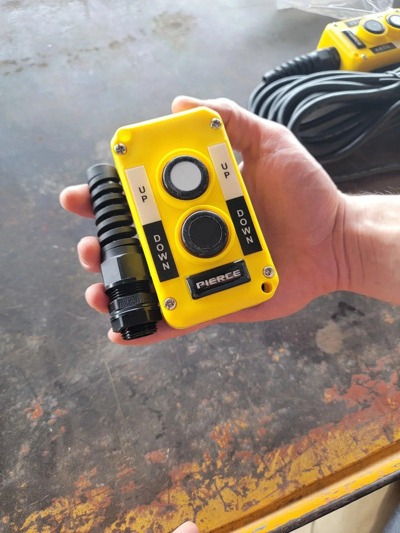 An Asetek Enterprise Company LTD Universal Momentary Pendant Control - 2 Button with UP and DOWN switches and a coiled black cable is held in hand, ideal for industrial use.