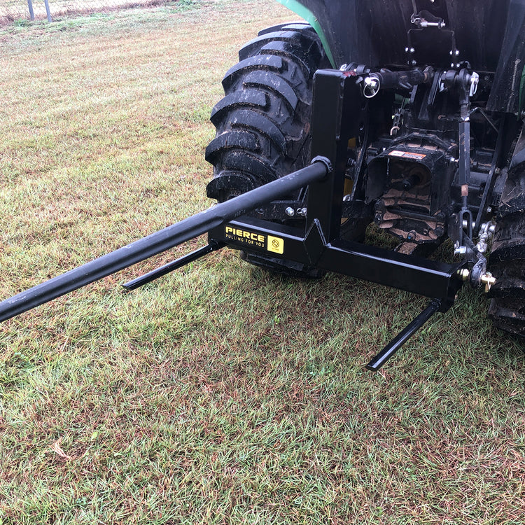 A PIERCE 3 Point Tractor Bale Spike with a black hitch attachment is set on the grassy field, perfect for handling round bales effortlessly.