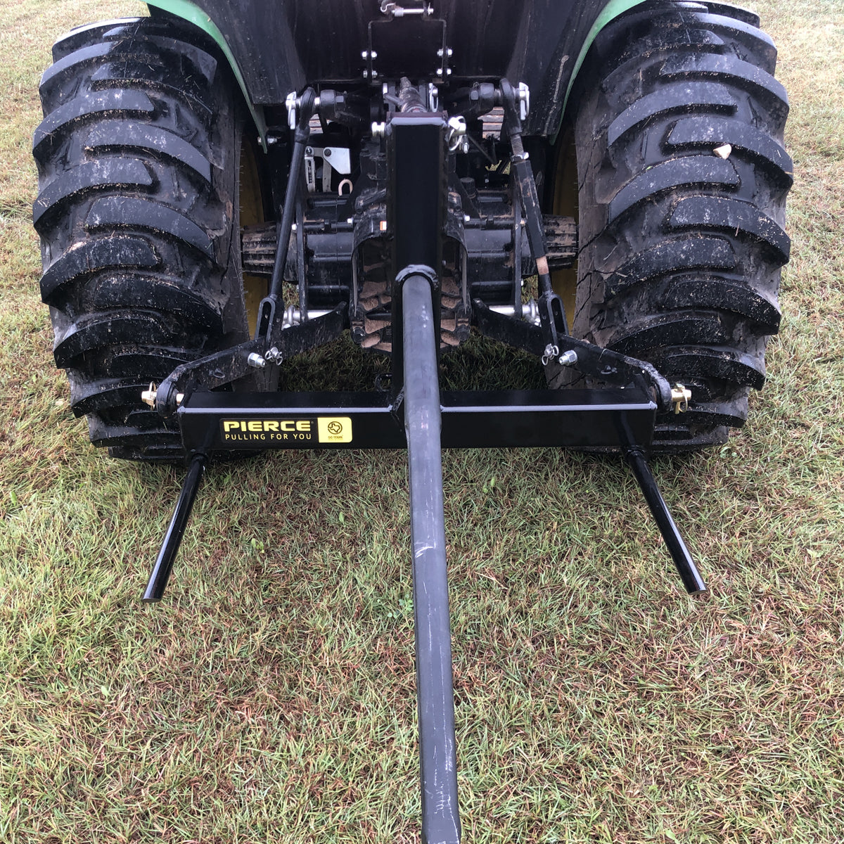 A rear view of a tractor parked on grass displays the PIERCE 3 Point Tractor Bale Spike, featuring a durable black towing frame made of high-quality steel, designed to handle round bales efficiently.