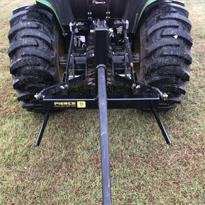A rear view of a tractor parked on grass displays the PIERCE 3 Point Tractor Bale Spike, featuring a durable black towing frame made of high-quality steel, designed to handle round bales efficiently.