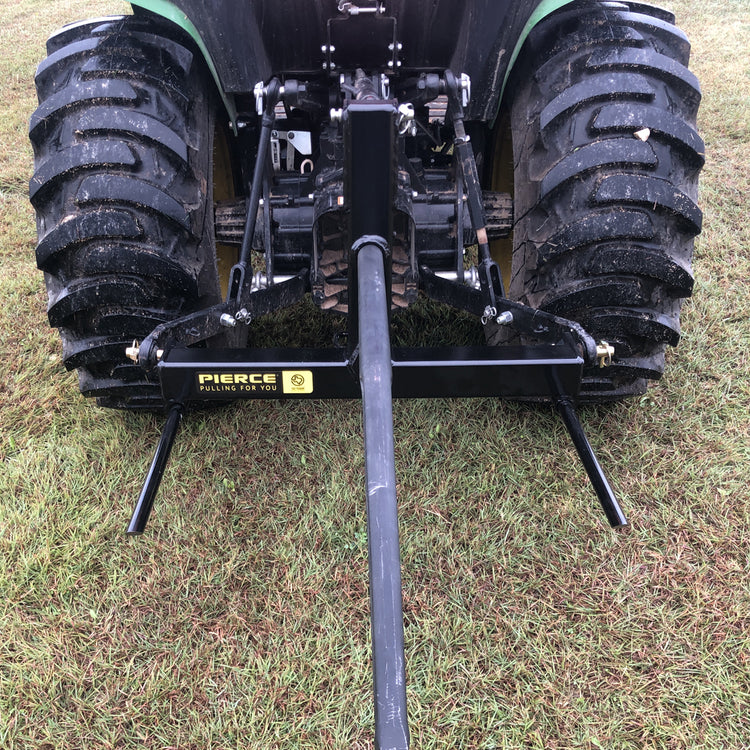 A rear view of a tractor parked on grass displays the PIERCE 3 Point Tractor Bale Spike, featuring a durable black towing frame made of high-quality steel, designed to handle round bales efficiently.