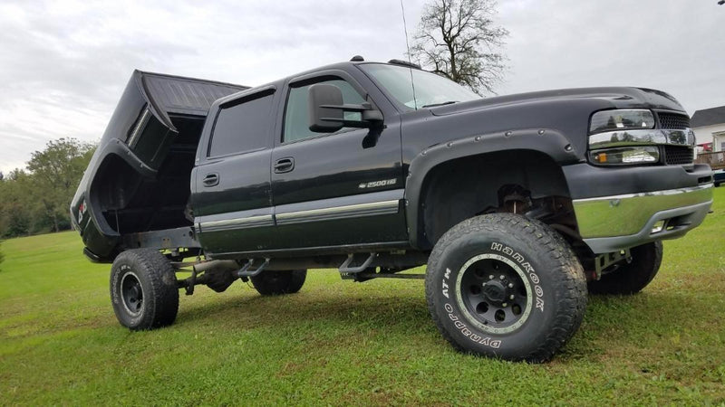 Black pickup truck with lifted suspension, parked on grass with its dump bed raised, features the PIERCE Factory Bed Dump Kit.
